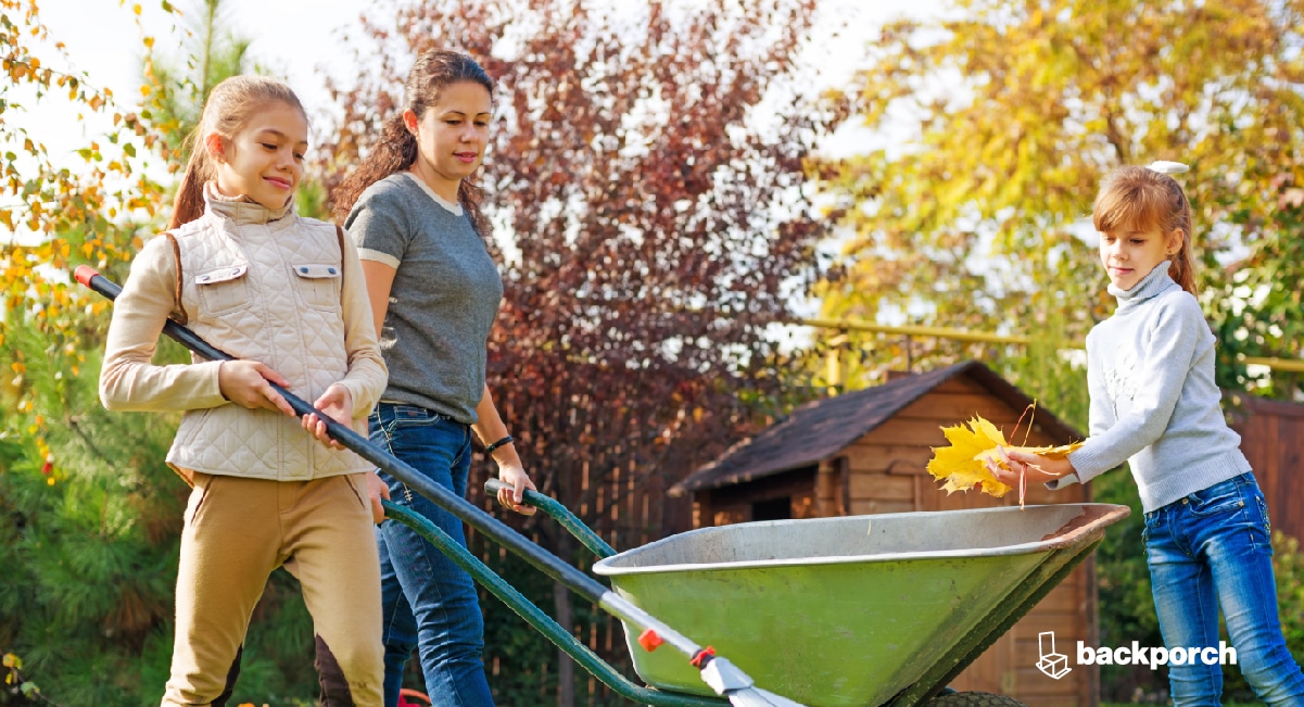 Three young girls loading leaves into a wheel barrow.