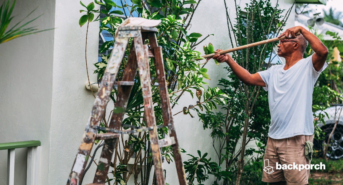A worker standing next to a stepladder is painting the exterior of a home.