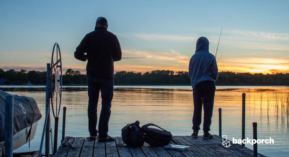 Two people fishing from the end of a dock at sunrise.