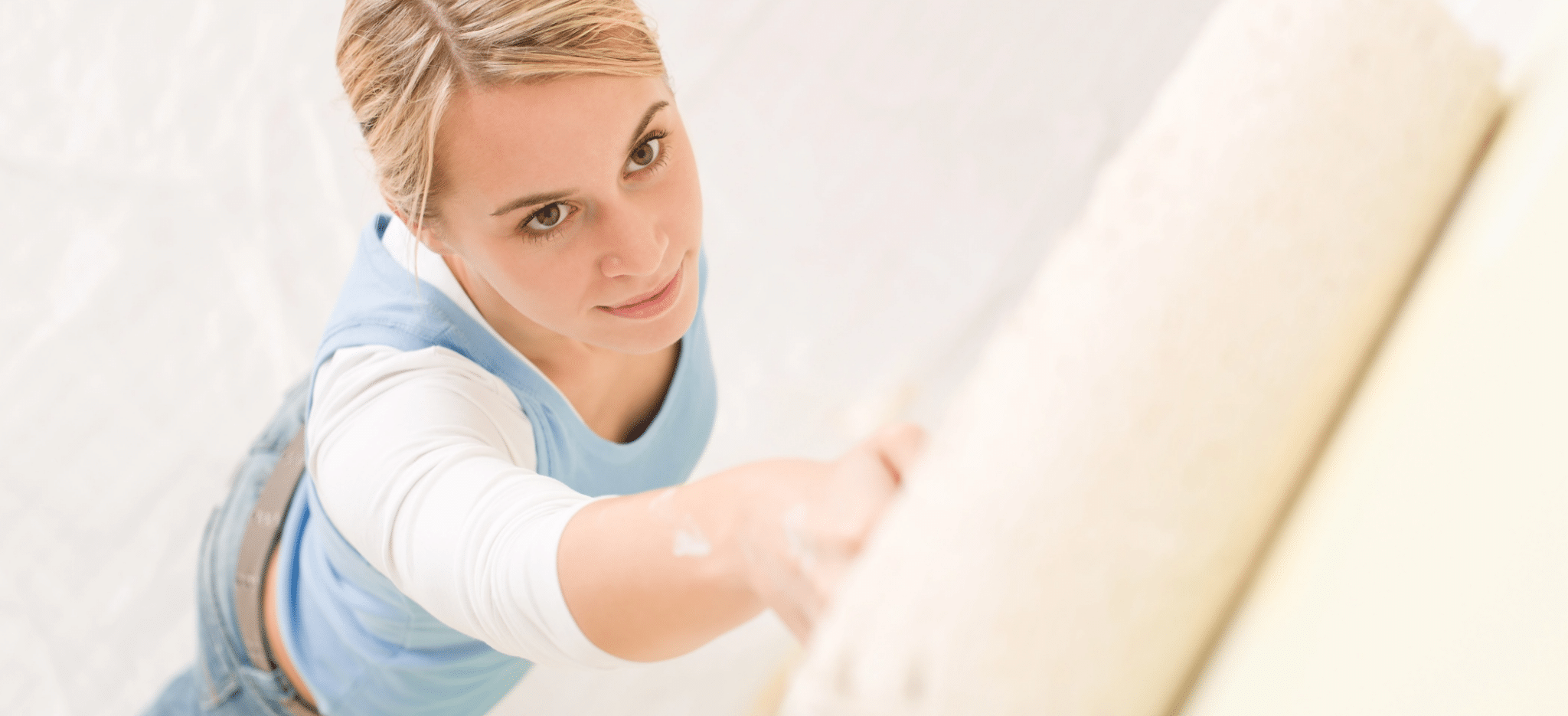 A woman painting a wall with a roller using white paint.