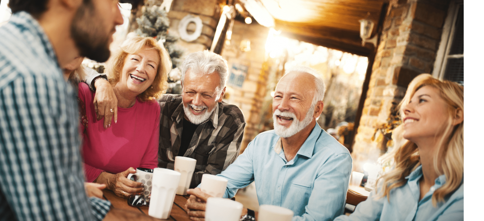 A group of smiling and laughing people sitting around a wooden table with drinks.