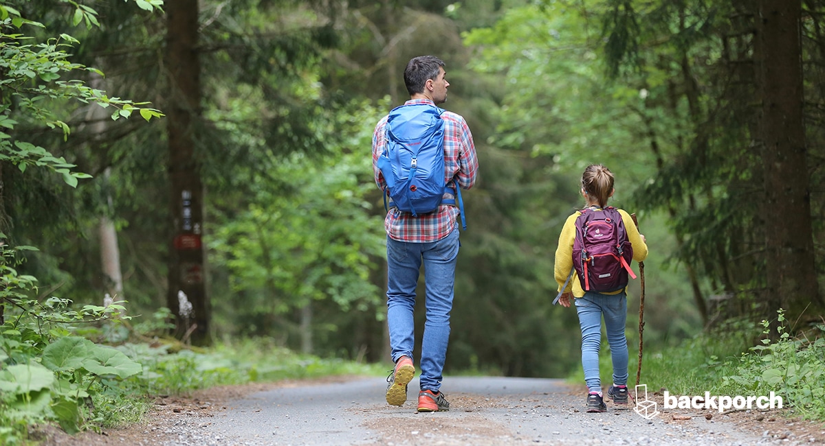 A man and a child walking down a path in the woods.